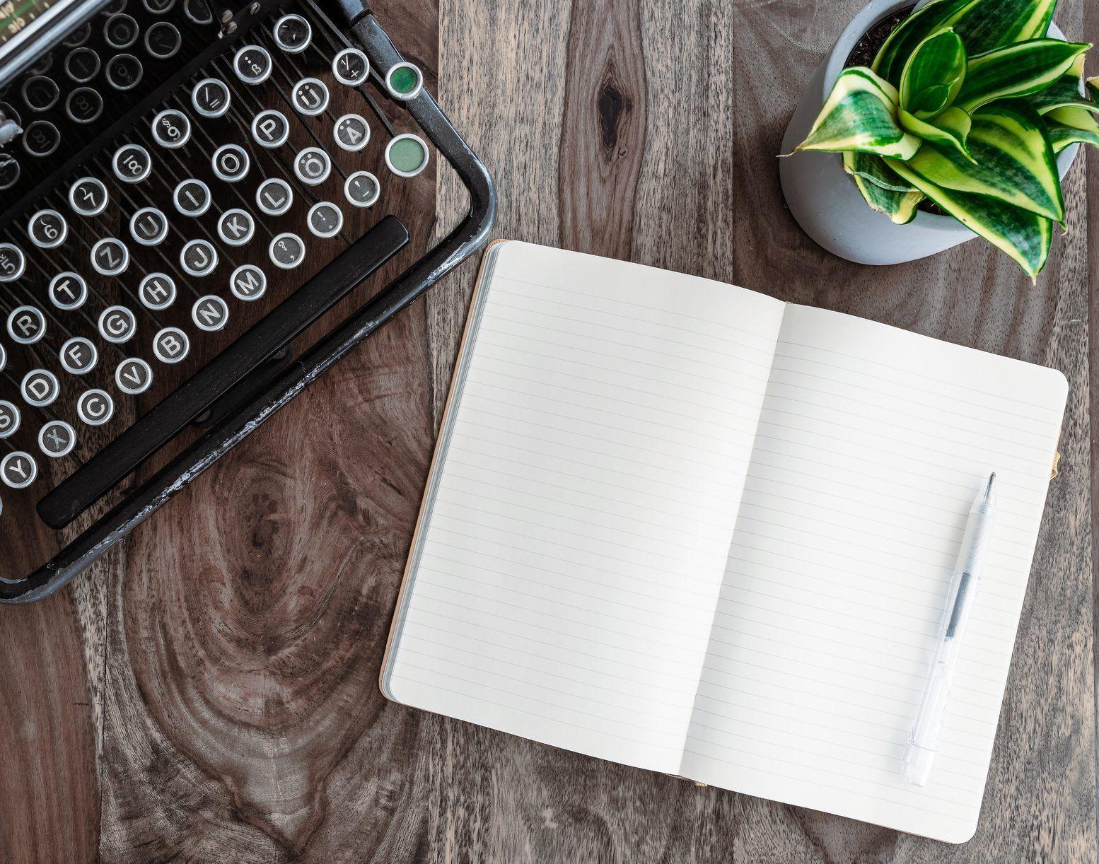 A writer typing on a laptop beside a notebook