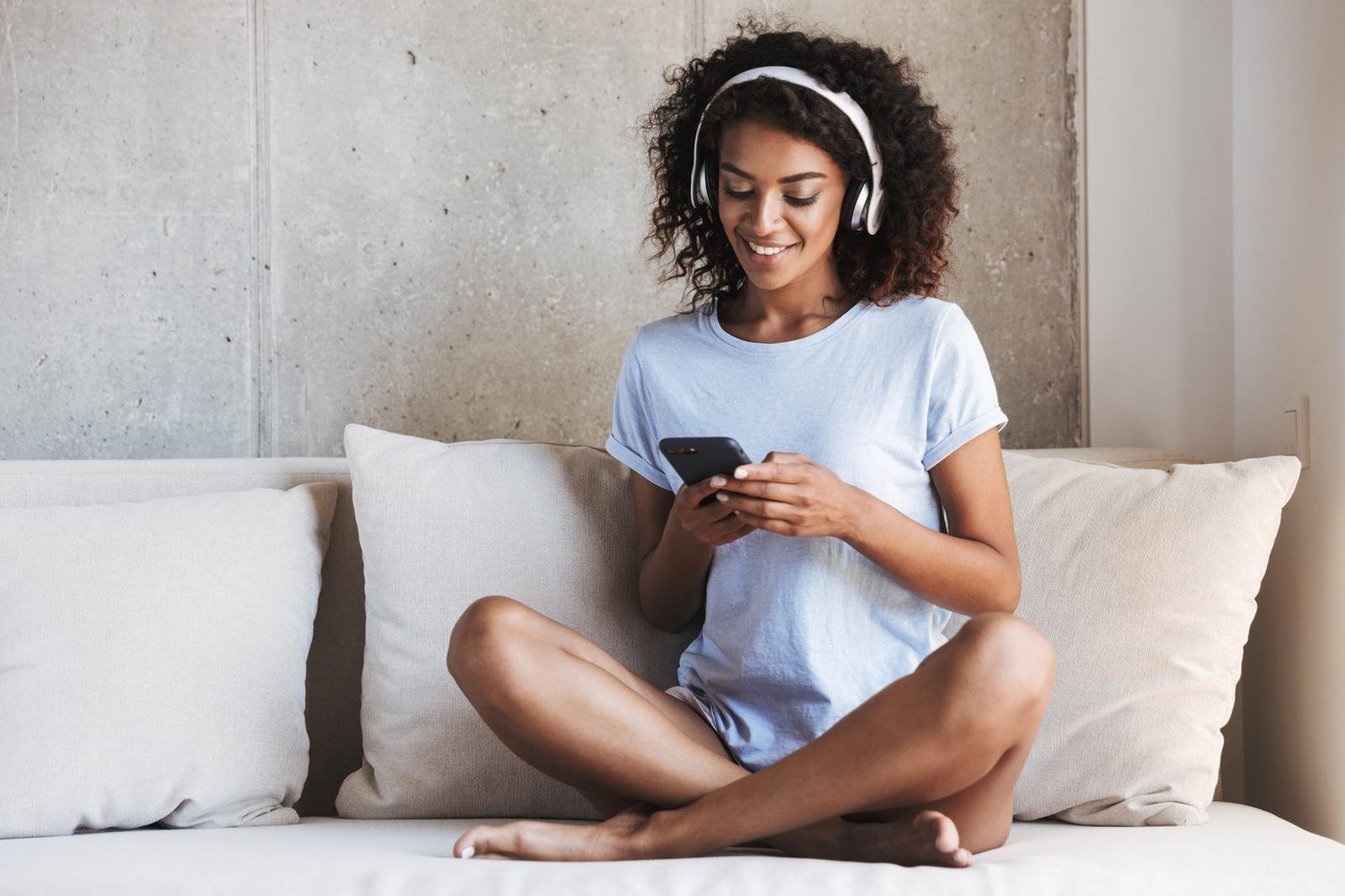 A smiling woman in headphones using an app on her phone
