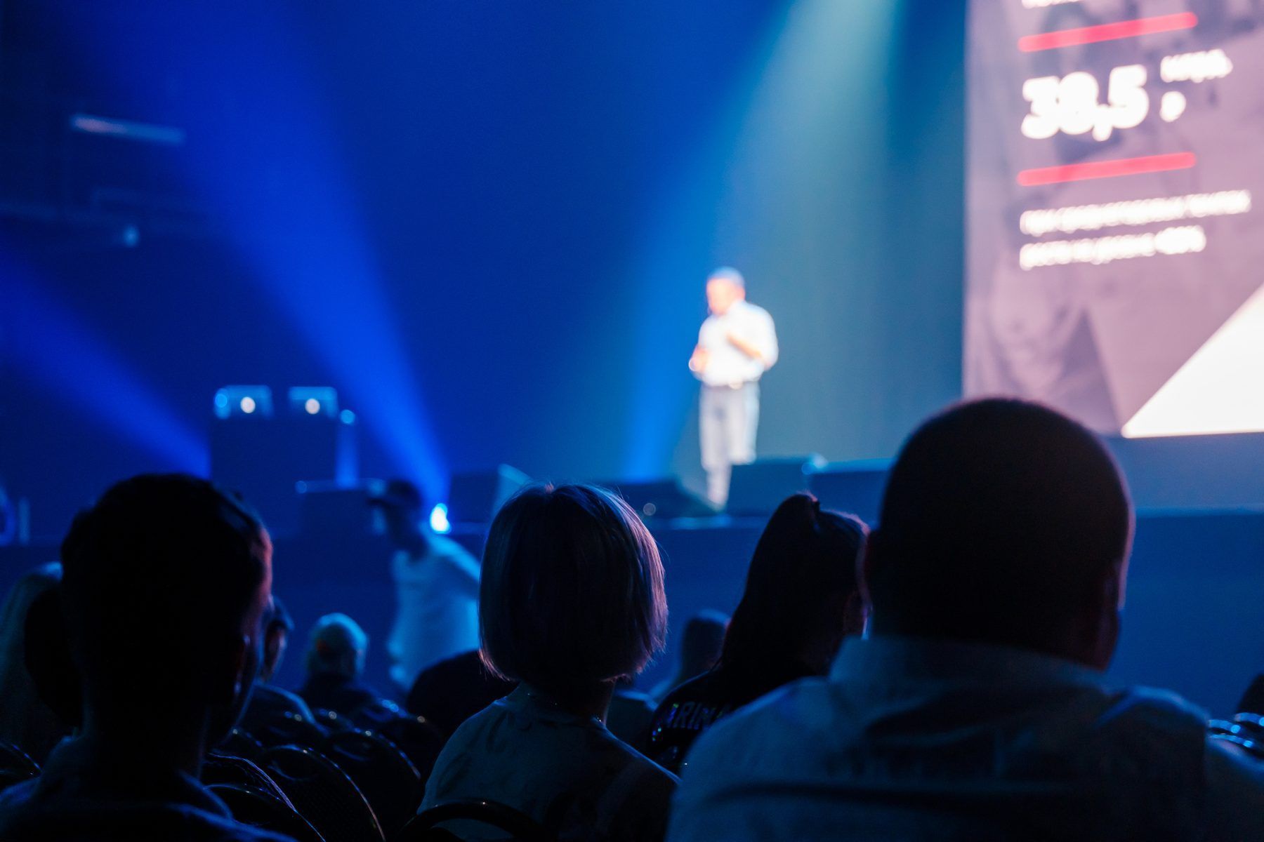 An audience watching a speaker on a lit stage